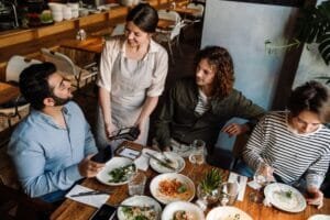 Why Swad is the Premier Indian Restaurant in West Vancouver. Cheerful indian man using a smartphone while paying the restaurant bill with contactless payment during a dinner party with friends.